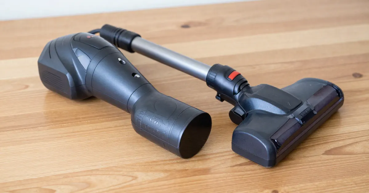 Illustration of a generic cordless stick vacuum taken apart on a wooden floor: motor body, wand and floor head laid side by side
