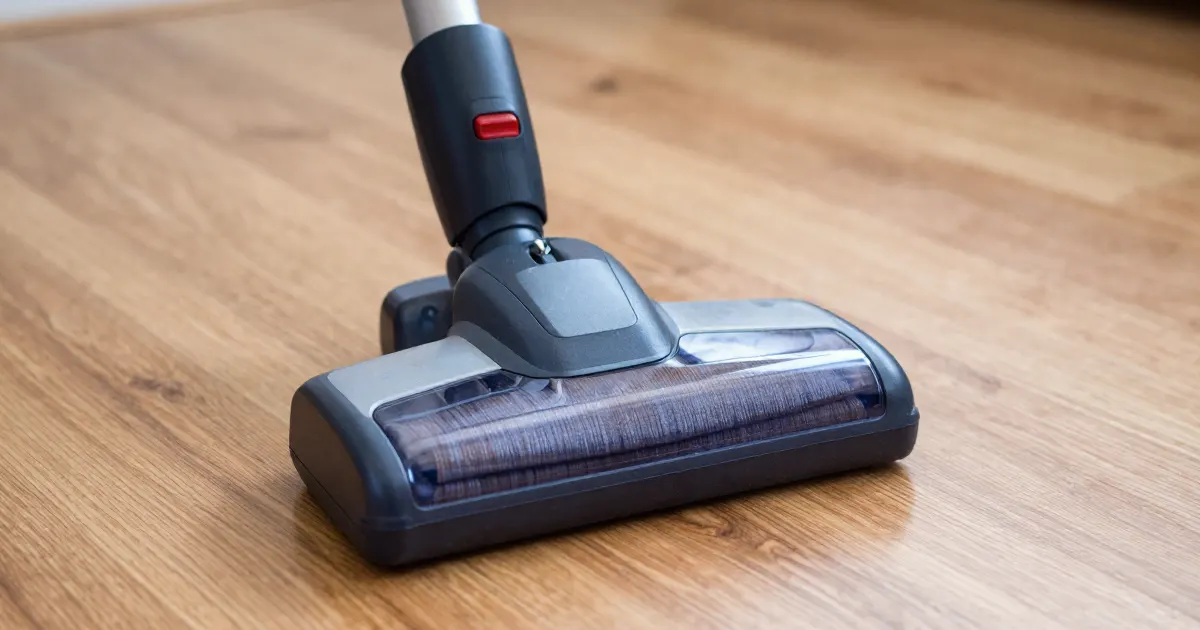 Illustration of a generic cordless vacuum floor head resting on a wooden floor, close-up of the brush bar housing