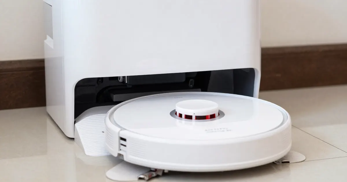 Illustration of a generic white robot vacuum mop parked at the open front of its white base station on a tiled floor