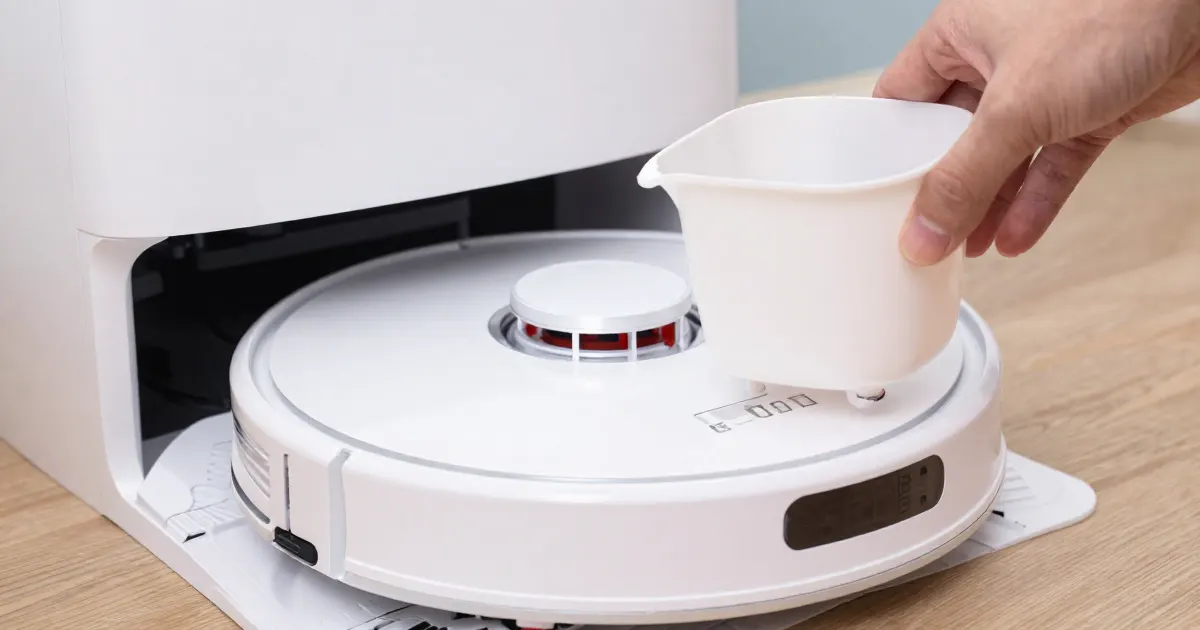 Illustration of a hand lifting the dust bin out of a generic white robot vacuum parked in its dock