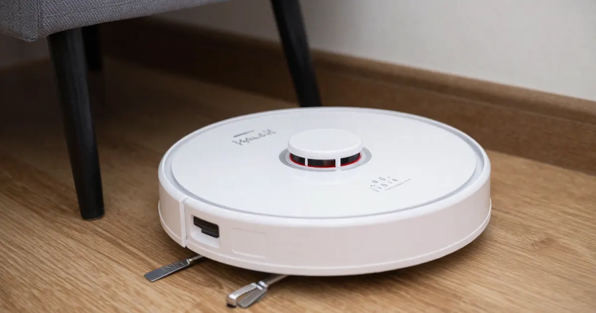 Illustration of a generic white robot vacuum on a wooden floor beside a chair leg