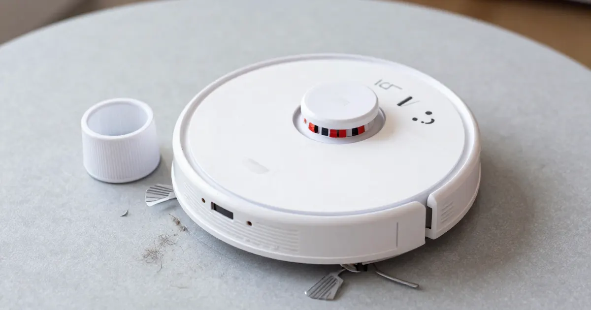 Illustration of a generic white robot vacuum on a grey rug beside a small white container and some debris