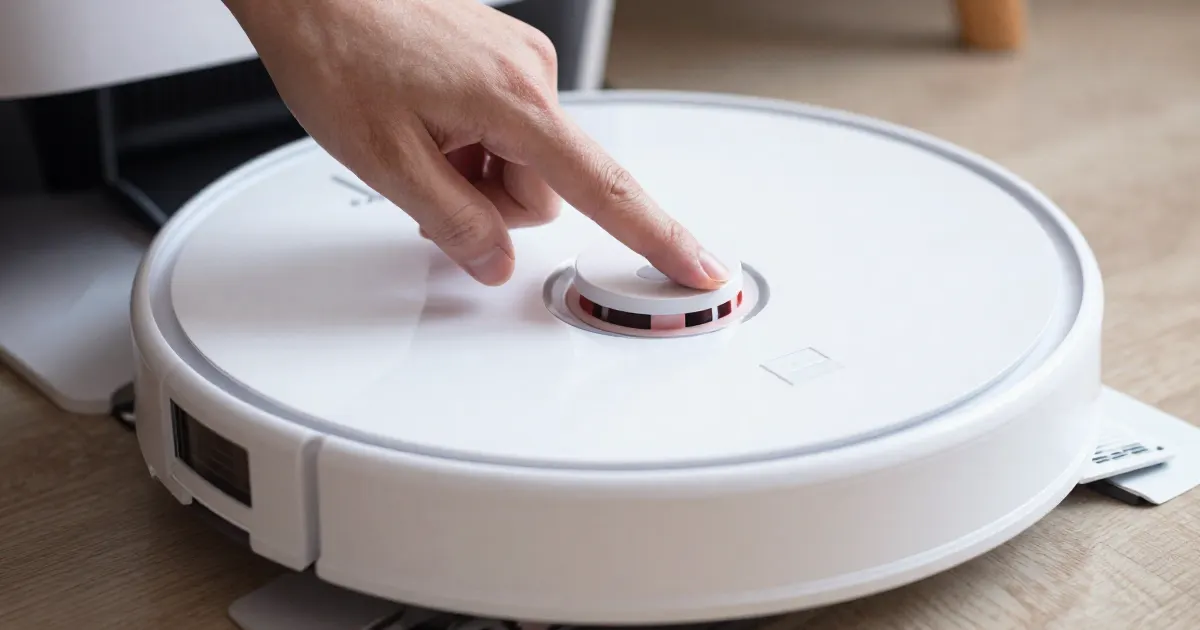 Illustration of a finger pressing the top button of a generic white robot vacuum