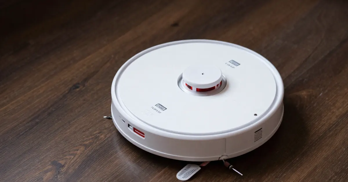 Illustration of a generic white robot vacuum sitting on a dark wooden floor