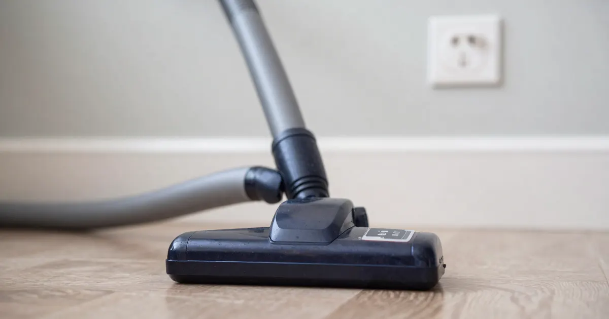 Illustration of a generic canister vacuum hose and floor head on a floor below a wall outlet